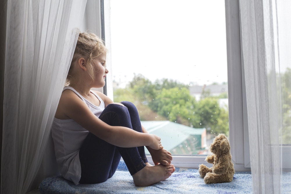 Little girl and teddy bear sitting by window