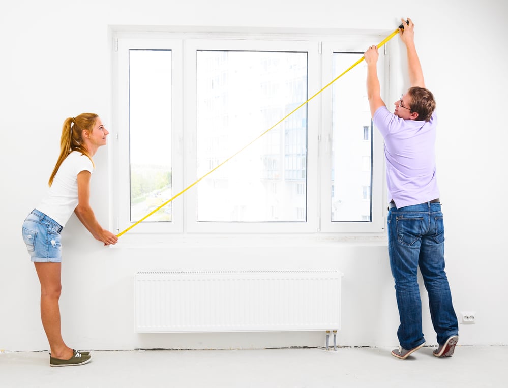 Young couple measuring a large window with a tape measure