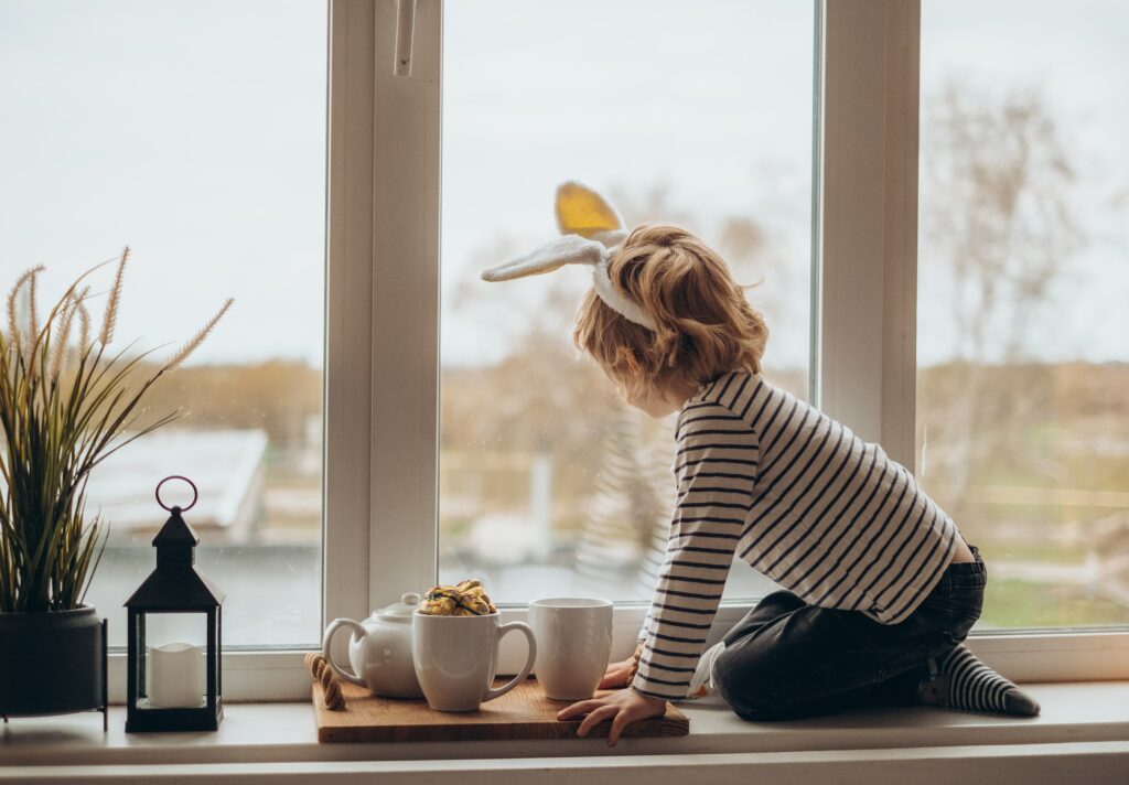 little boy looking out window while wearing bunny ears